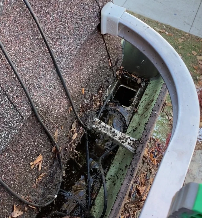 A before shot of a dirty gutter with mud, water, and small leaves is shown. Leaves and mud stain the bottom row of the roof's shingles as well.